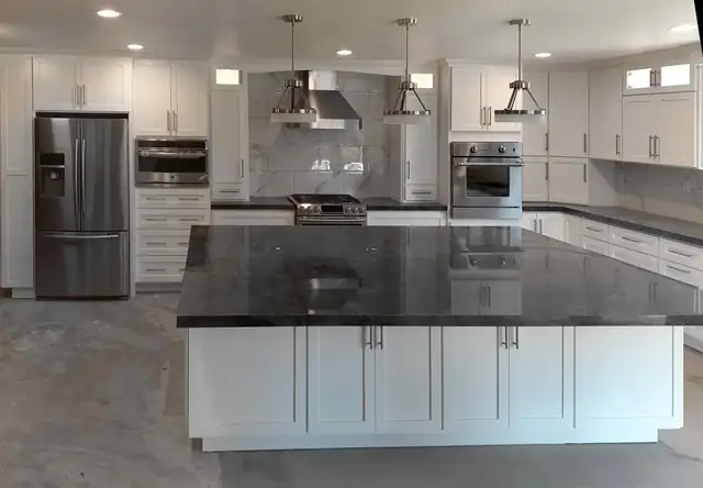 White Shaker kitchen with a large dark stone-topped island, stainless appliances and three pendant lights