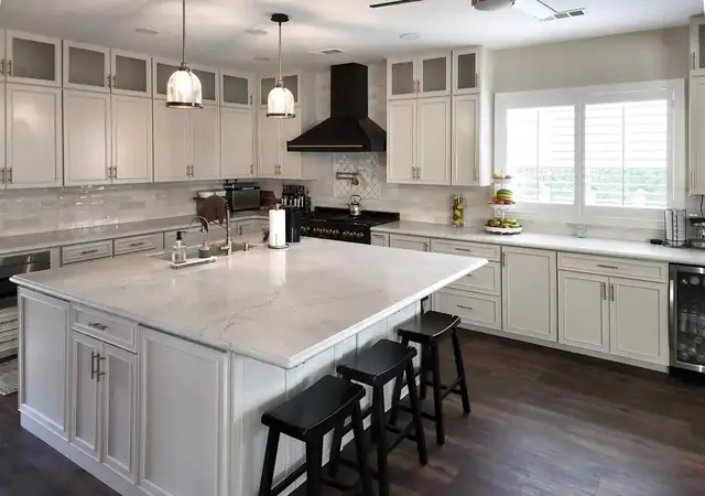 White Shaker kitchen in Temecula with frosted glass uppers, black chimney hood, quartz island and black saddle stools