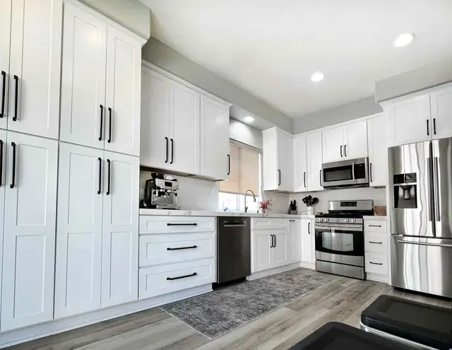 White shaker kitchen with tall pantry cabinets, matte black pulls, stainless appliances and wood-look floors