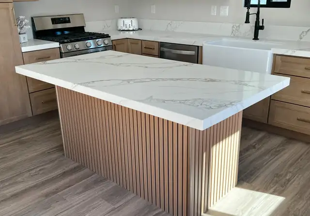 Kitchen island with fluted wood panels, white quartz top, farmhouse sink and wood-tone cabinets
